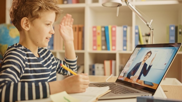 Foto slimme kleine jongen gebruikt laptop voor videogesprek met zijn leraar scherm toont online lezing met leraar verwelkomt de student met zwaaiend gebaar jongen antwoordt met ee distance learning