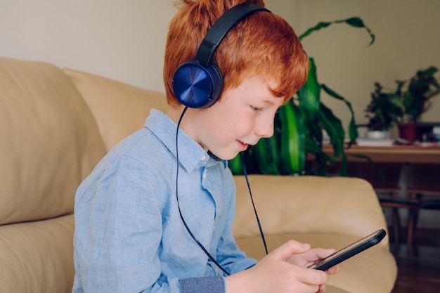 Slimme kleine jongen luisteren naar muziek met mobiele telefoon geluiddichte hoofdtelefoon thuis.