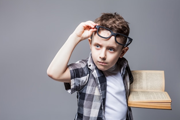 Slimme leerling in glazen met leerboek in handen, studio fotoshoot. Kinderopvoeding concept