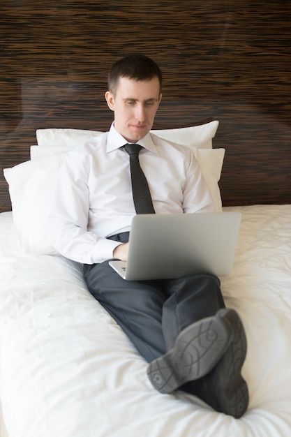 Slimme man liggend in bed te typen op een laptop