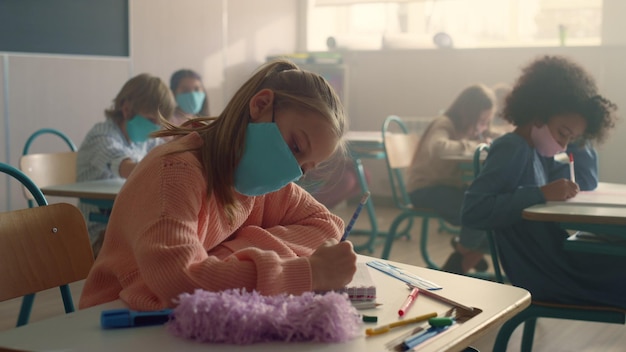 Foto slimme meisje in medisch masker leert in de klas tijdens de coronaviruspandemie