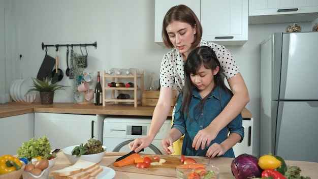 Slimme moeder en Aziatisch meisje koken samen en hakken groenten Pedagogie