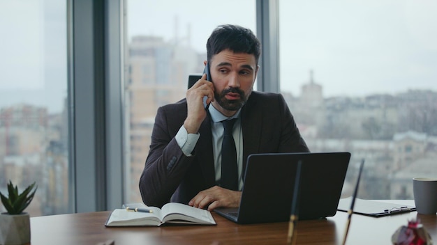 Slimme regisseur praat met mobiele telefoon zit op het bureau met laptop close-up werkoproep