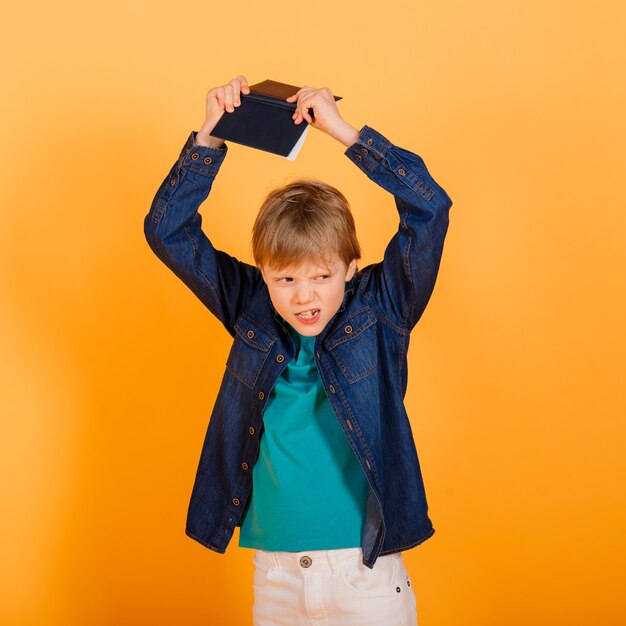 Slimme roodharige jonge schooljongen met notitieboekje geïsoleerd op gele achtergrond, studio