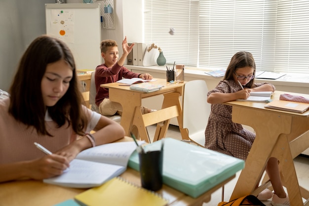 Slimme schooljongen die hand opsteekt tussen zijn klasgenoten