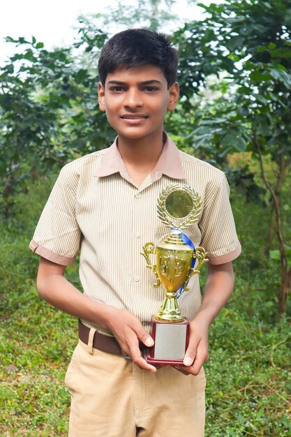 Slimme schooljongen die zijn trofee opheft als winnaar in schoolcompetitie