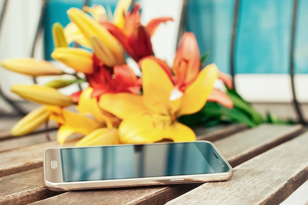 Slimme telefoon op vintage grunge houten tafel wazig gele en rode bloemen op de achtergrond