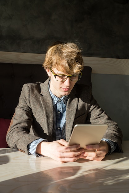 Slimme toevallige jongere in het lezen van brillen aan tafel zitten en surfen op draagbare computer bij koffiepauze