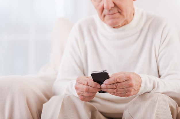 Slimme volwassenheid. close-up van senior man die mobiele telefoon vasthoudt terwijl hij in de stoel zit