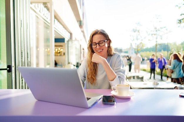 Slimme vrouw in glazen zitten in café met behulp van laptop