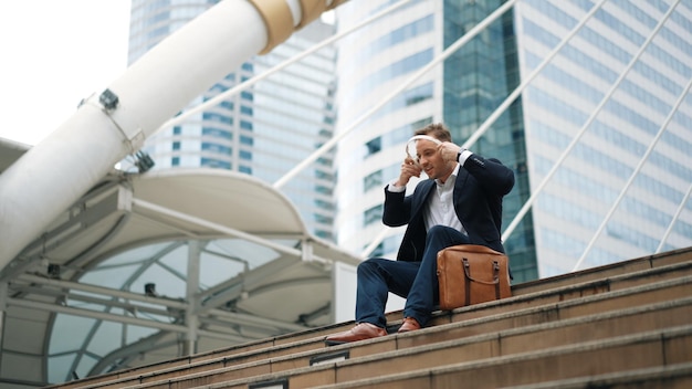Foto slimme zakenman draagt koptelefoon terwijl hij op de trap zit in de stedelijke stad urbane