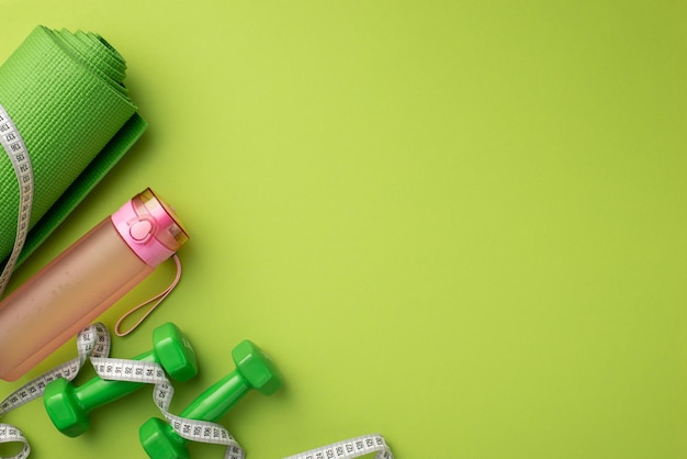 Slimming concept Top view photo of sports mat tape measure pink bottle of water and dumbbells on isolated green background with empty space