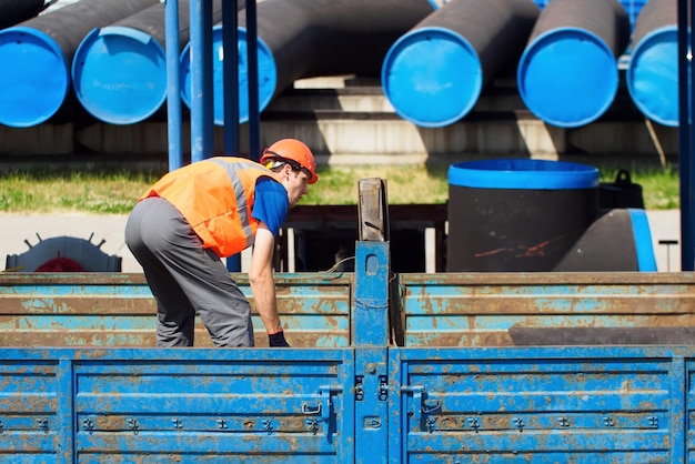 Slinger in orange hard hat and construction vest works outside on summer day worker unloads pipes for gasification real workflow