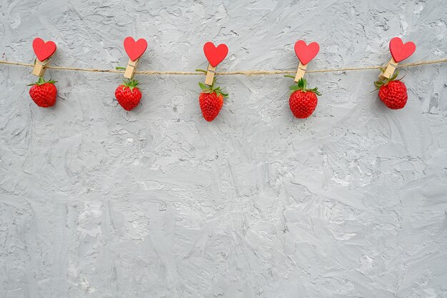 Slinger van rode rijpe aardbeien die op houten wasknijper met harten op kabeltouw hangen