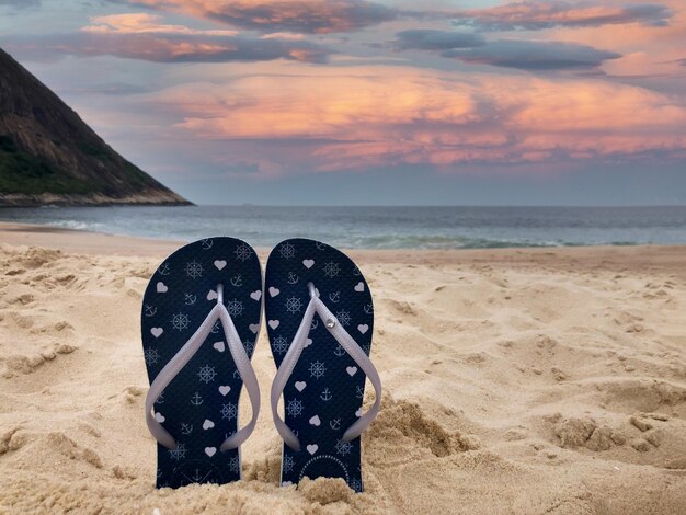 Slippers op het strandzand Zee en zonsondergang in de bergen voor het strand van Rio de Janeiro