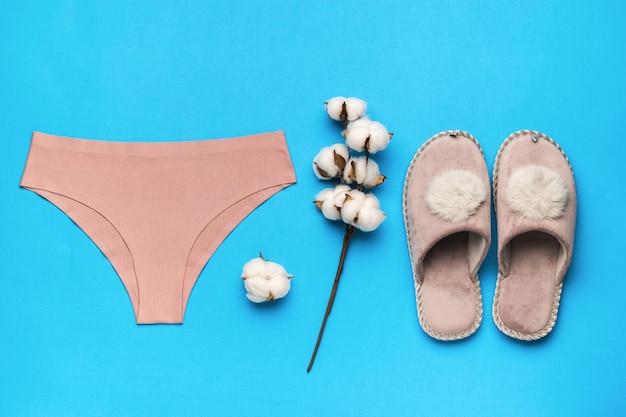 Slippers panties and a sprig of cotton on a blue background Minimal concept of women's accessories