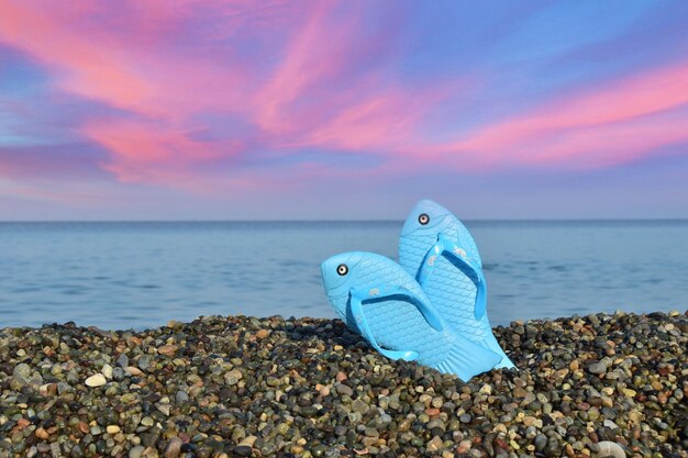 Slippers in pebbles against sea during sunset