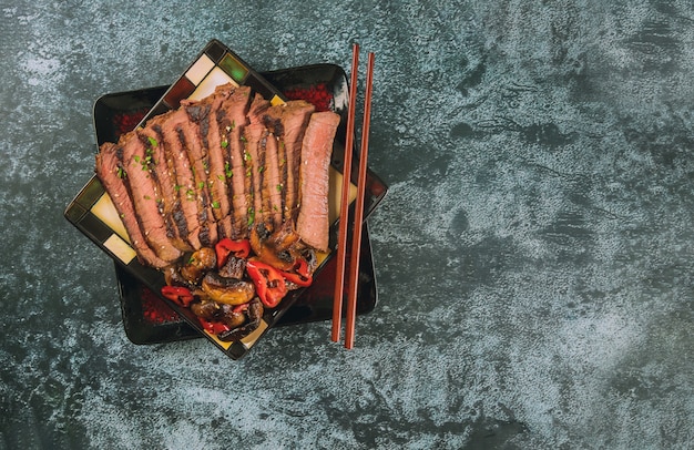 Slised grilled beef on black plate.