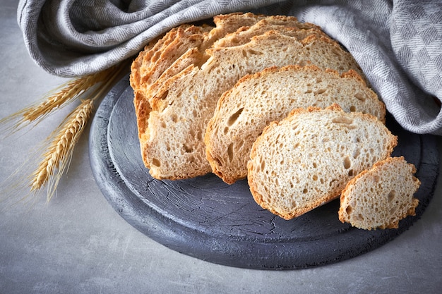 Slliced white round bread with wheat ears on gray stone wall