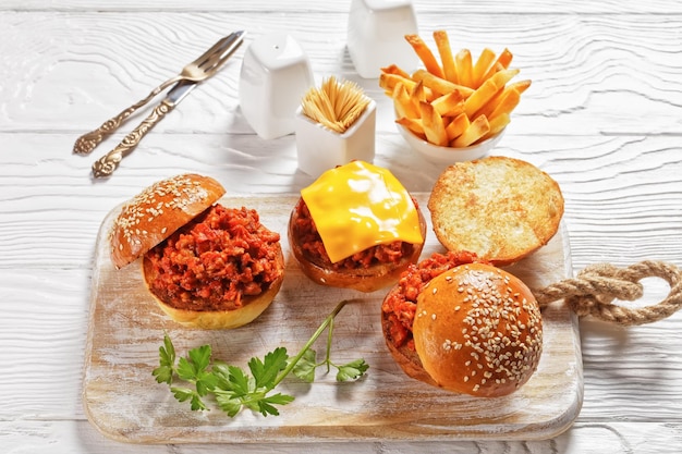 Сэндвичи Sloppy Joe на булочках с булочками, подаются с картофелем фри на белой деревянной доске, крупный план, американская кухня