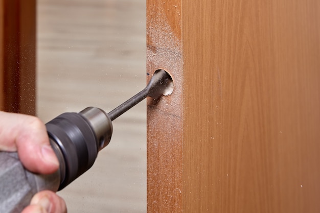 Slotenmaker gebruikt een platte bit om hout te boren bij het boren van een gat voor vergrendeling.