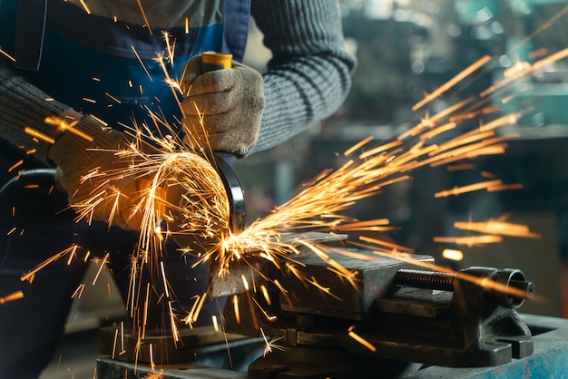 Slotenmaker in speciale kleding en bril werkt in productie. Metaalbewerking met haakse slijper. Vonken in metaalbewerking.