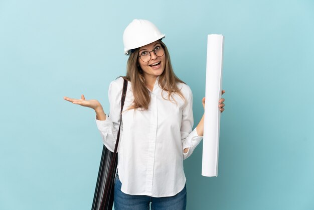 Photo slovak architect girl holding blueprints isolated on blue wall with shocked facial expression