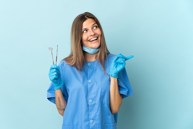 슬로바키아어 치과 의사는 손가락을 들어 올리면서 솔루션을 실현하려는 파란색 배경에 고립 된 도구를 들고