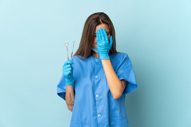 Slovak dentist holding tools isolated on blue wall with tired and sick expression