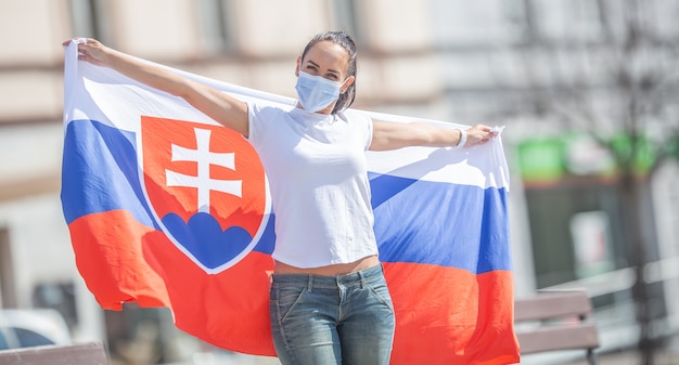 Фото Словацкая фанатка в маске держит за спиной на улице флаг.