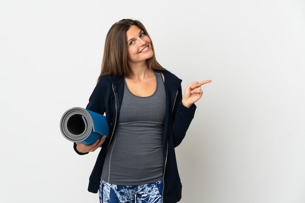 Slovak girl going to yoga classes isolated on white wall pointing finger to the side