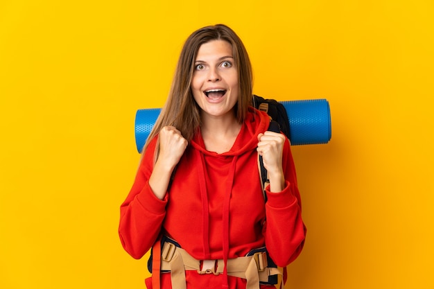 Slovak mountaineer woman with a big backpack isolated on yellow background celebrating a victory in winner position