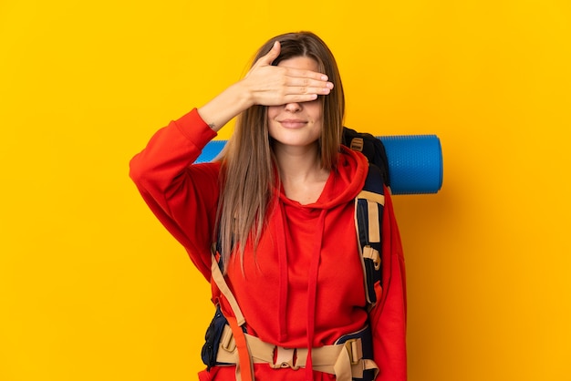 Slovak mountaineer woman with a big backpack isolated on yellow background covering eyes by hands. Do not want to see something