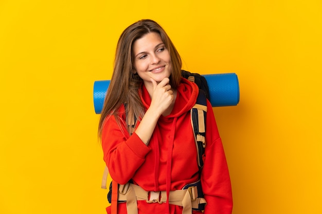 Slovak mountaineer woman with a big backpack isolated on yellow background looking to the side and smiling