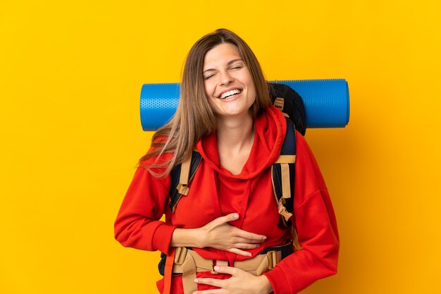 Slovak mountaineer woman with a big backpack isolated on yellow background smiling a lot