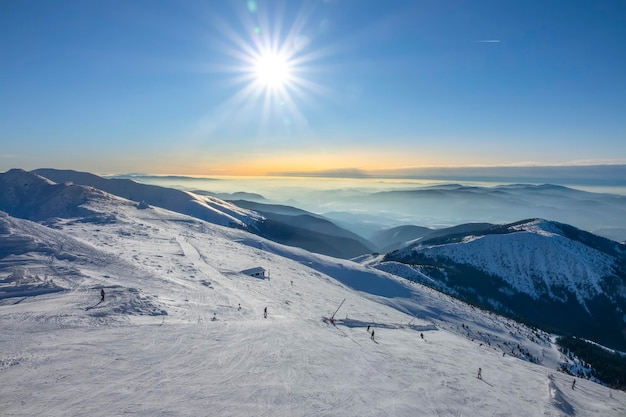 Slovakia. Winter ski resort Jasna. Bright sun in the blue sky over the ski slope. Mountain peaks and fog on the horizon