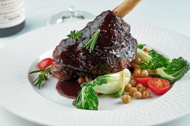 Slow cooked lamb Shank in wine sauce on a white plate on a white tablecloth