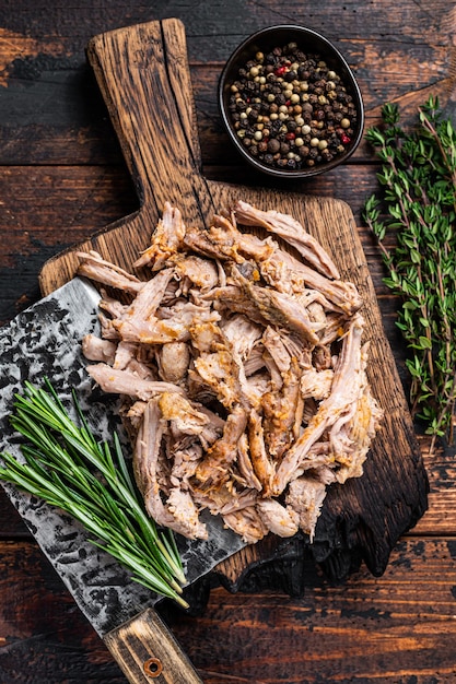 Slow cooked  puilled pork meat on a wooden board with butcher cleaver. Dark wooden background. Top view.