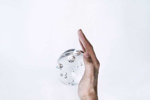 Photo slow motion of cropped hand holding water bubble against white background