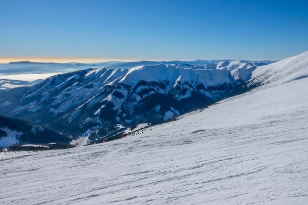 Slowakije. Winterskigebied Jasna. Zonnig weer en blauwe lucht over een lege brede skipiste. Bergtoppen en mist aan de horizon