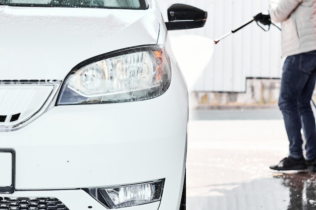 Sluit bemant omhoog hand die een witte auto wassen gebruikend hogedrukwater. Zelf wassen van auto's