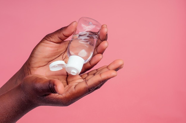 Sluit de handen van een vrouw met een donkere huid die alcoholgel in de hand roze studioachtergrond toepast.