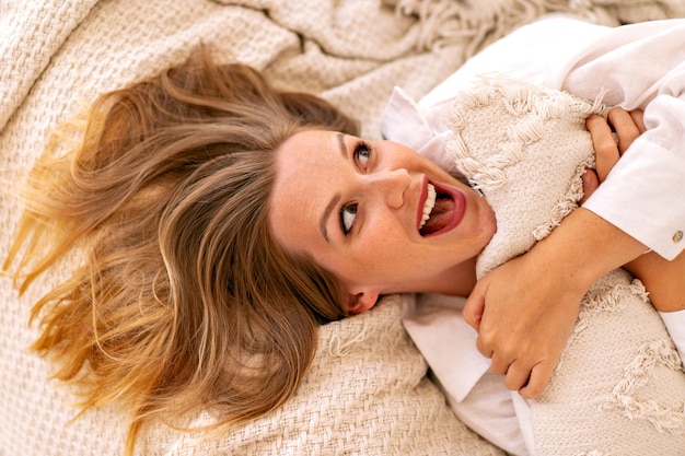 Foto sluit het ochtendportret van een mooie blonde vrouw die op het bed ligt en een perfecte ontspannende tijd alleen heeft