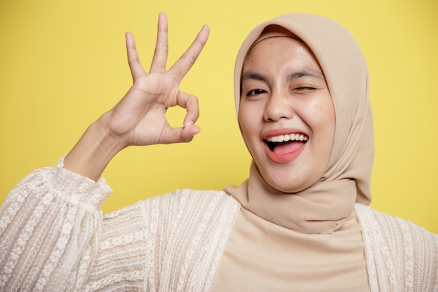 Sluit jonge hijab-vrouwen gelukkig en toon het OK-teken dat op een gele achtergrond wordt geïsoleerd