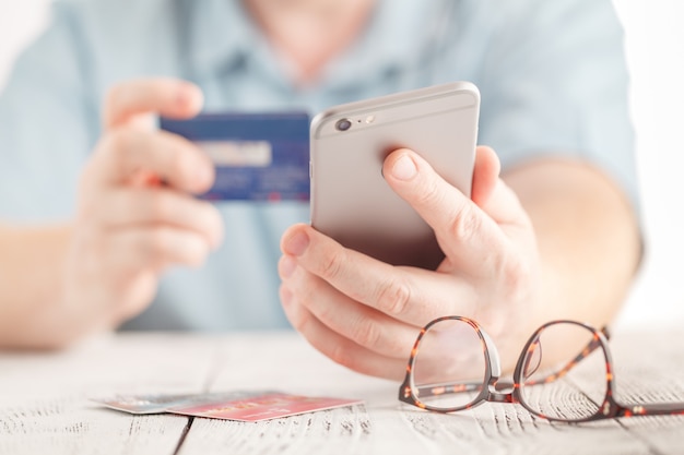 Sluit mannelijke handen omhoog houdend creditcard en gebruikend mobiele slimme telefoon om online te winkelen