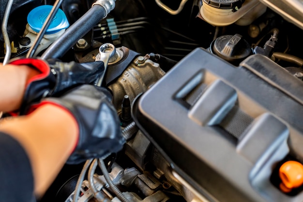 Sluit omhoog, Aziatische mensen automonteur die een moersleutel en een schroevedraaier gebruiken aan werkende dienstauto in garage.