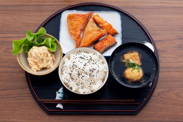 Sluit omhoog de Japanse zalm van voedseltiyaki met rijstreeks die op houten lijst wordt gediend.