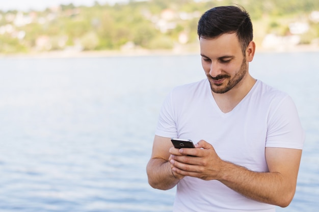 Sluit omhoog de knappe jonge mens die slimme telefoon met behulp van terwijl in openlucht status