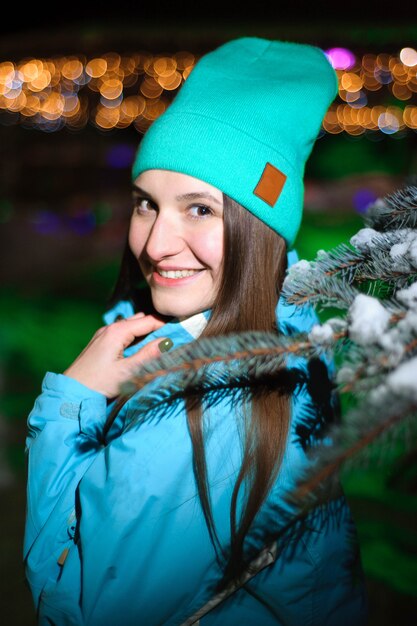 Sluit omhoog De winterportret van een jonge glimlachende vrouw in een blauwe hoed bij nacht.