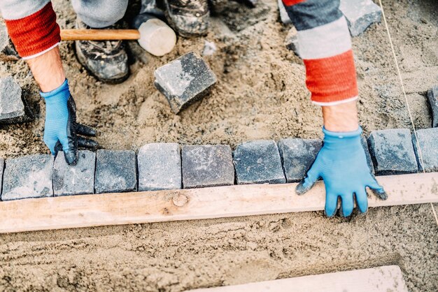 Foto sluit omhoog details van bouwvakker die granietkei op wegbestrating legt